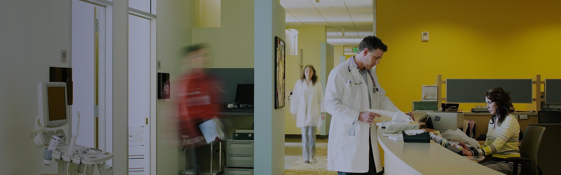 Image of a hospital reception desk with staff walking along the corridor