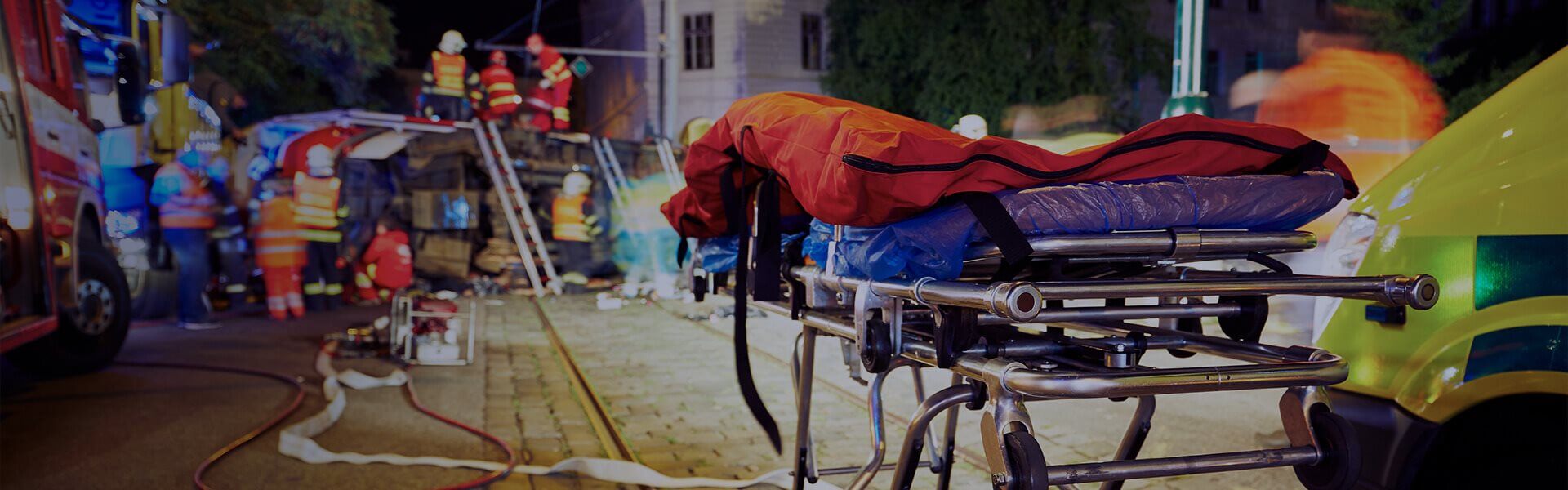 Image of an Ambulance stretcher, with fire services exploring a site in the background
